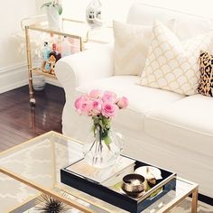 a living room with white couches and pink roses in a vase on the coffee table