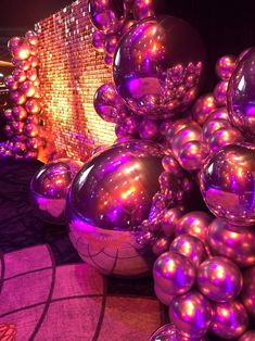 many shiny balls are stacked on top of each other in front of a colorful wall