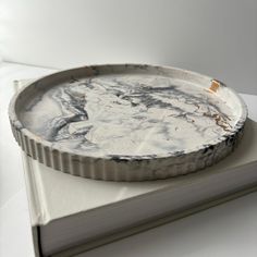 a round metal tray sitting on top of a white table next to an open book