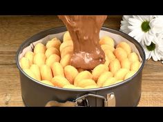 a person pouring chocolate into a tin filled with doughnuts and daisies on a wooden table