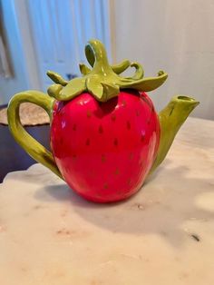 a ceramic strawberry teapot sitting on top of a table