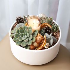 a white bowl filled with succulents and candles on top of a table