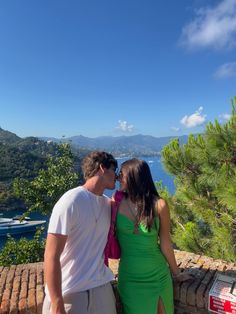 a man and woman standing next to each other on top of a hill near the ocean