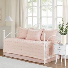 a white daybed with pink bedding and pillows in a room next to a window