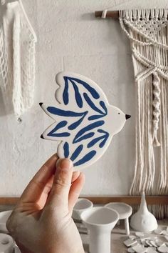 a hand holding up a blue and white fish decal in front of a wall hanging