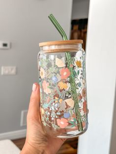 a hand holding a mason jar with flowers painted on the side and a straw sticking out of it