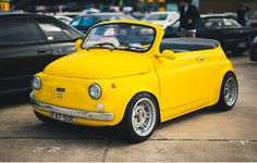 a small yellow car parked next to other cars