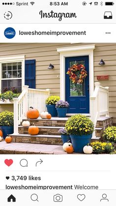 front porch decorated for fall with pumpkins and flowers on the steps next to blue door