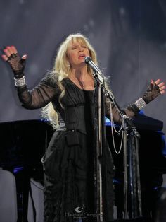 a woman standing in front of a microphone on top of a stage next to a piano