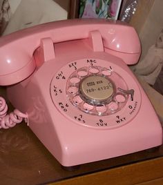 an old pink phone sitting on top of a desk next to a framed photo and telephone cord