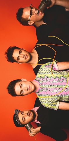 three men standing next to each other in front of a red wall with wires hanging from them