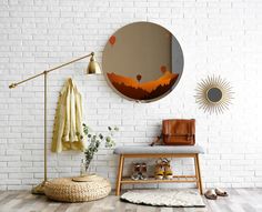 a white brick wall with a round mirror on the wall and a bench in front of it