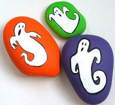 three painted rocks with ghost faces on them, one is orange and the other is green