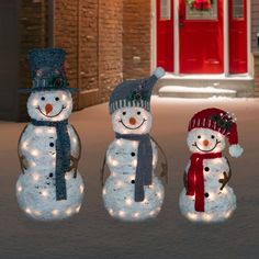 three snowmen with hats and scarves are standing in front of a red door