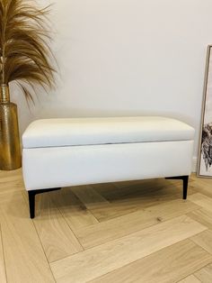 a white bench sitting on top of a hard wood floor next to a potted plant