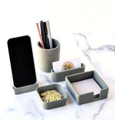 three office supplies sitting on top of a white counter next to a cell phone and pen holder