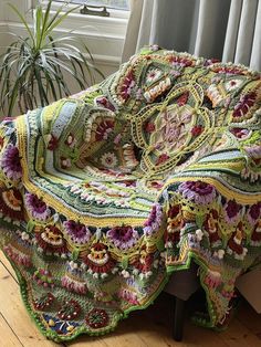 a crocheted blanket is sitting on a chair next to a potted plant