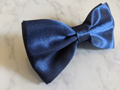 Upgrade your wardrobe in style with this stunning blue satin bow tie. Perfect gift for him, this unique adjustable bow tie will elevate your style for any occasion including weddings, birthdays and anniversaries. Comes pre-tied. Dapper Blue Satin Bow, Dapper Blue Bow For Black Tie Events, Blue Bow Tie For Black Tie Events, Classic Blue Satin Bow Tie, Blue Satin Bow Tie, Blue Standard Bow Tie For Black Tie Events, Blue Bow With Bow Tie Back For Wedding, Blue Suit And Tie Accessories For Black Tie Events, Blue Bow Tie For Wedding