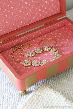 an open pink box with jewelry inside on a white tableclothed surface next to a pair of gold - plated bracelets