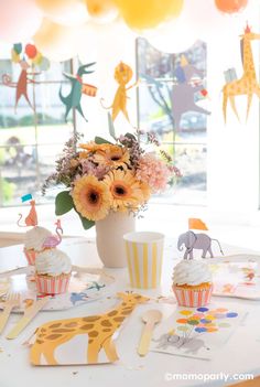 a white table topped with cupcakes and paper cutouts next to a vase filled with flowers