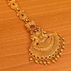 an ornate gold necklace with red stones on top of a wooden table and wood floor