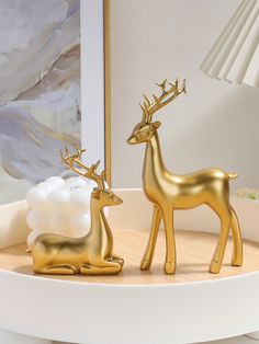 two golden deer figurines sitting on top of a white table next to a lamp