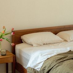 a bed with white sheets and pillows next to a small table with flowers on it