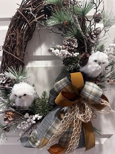 a wreath with two white dogs on it and pine cones, evergreens, and berries