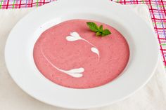 a white bowl filled with soup on top of a pink table cloth next to a knife and fork