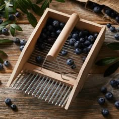 a wooden box filled with blueberries on top of a table next to green leaves