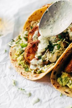 two tacos with chicken, lettuce and sauce being spooned into them