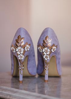 a pair of purple high heeled shoes with gold and white flowers on the toes