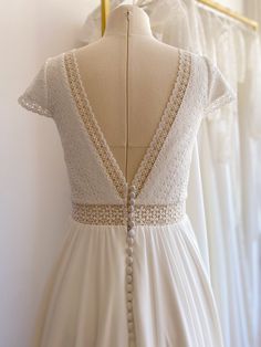 the back of a wedding dress hanging on a mannequin in front of white dresses