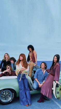 group of people sitting on top of an old car in front of the ocean with luggage