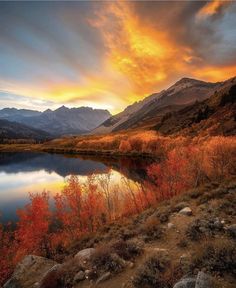 a beautiful sunset over a mountain lake with red and yellow trees in the foreground