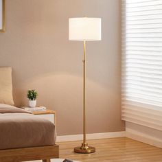 a living room with a bed and a lamp on the floor in front of a window