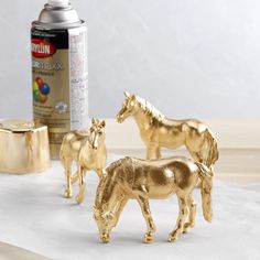 three gold horse figurines next to a can of spray paint on a table