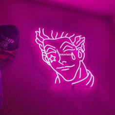 a pink neon sign with the image of a man's head on it, next to a purple hat