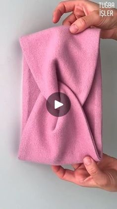 two hands holding a pink towel with a video button on the front and back of it