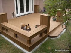 a dog laying on top of a wooden deck next to a tree and grass area