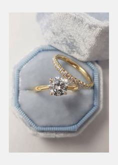 two gold engagement rings sitting in a blue velvet ring box with white and yellow diamonds on top