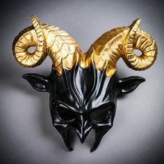 a black and gold mask with horns on it's face, against a gray background