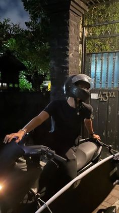 a man riding on the back of a motorcycle next to a gate at night time