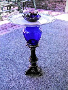 a blue glass bowl sitting on top of a metal stand in front of a table