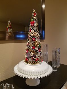 a decorated christmas tree sitting on top of a white cake plate next to crystal glasses