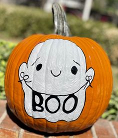 a pumpkin with a ghost face painted on it sitting on a brick surface in front of some bushes