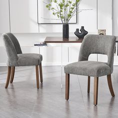 two gray chairs sitting at a table in front of a vase