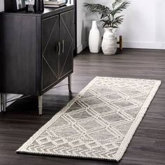 a white rug on top of a wooden floor next to a cabinet and vases