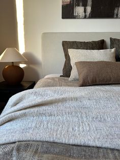 a bed with two lamps on either side of it and a painting above the headboard