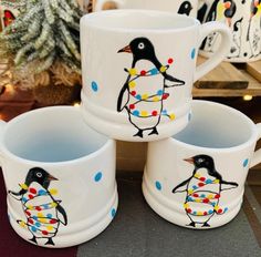 three mugs with penguins painted on them sitting next to a potted christmas tree